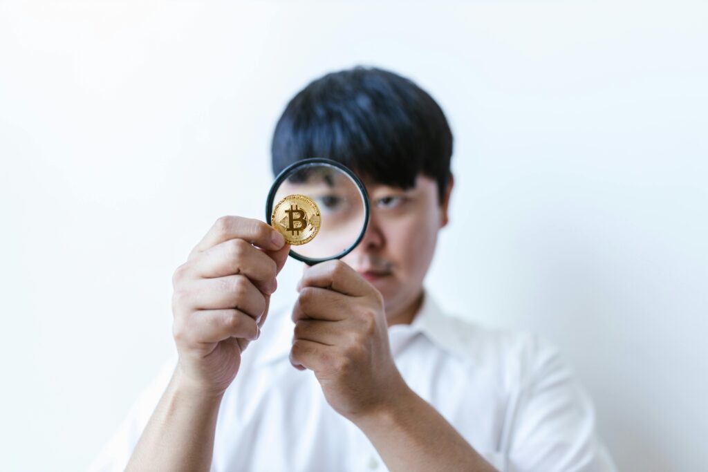 Close-up of a man examining a Bitcoin coin with a magnifying glass, symbolizing cryptocurrency analysis.