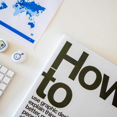 Stylish desk setup with a how-to book, keyboard, and world map on paper.